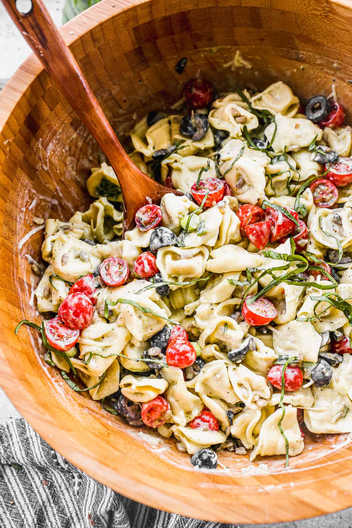 A wooden bowl filled with Pesto Tortellini salad, ready to serve.