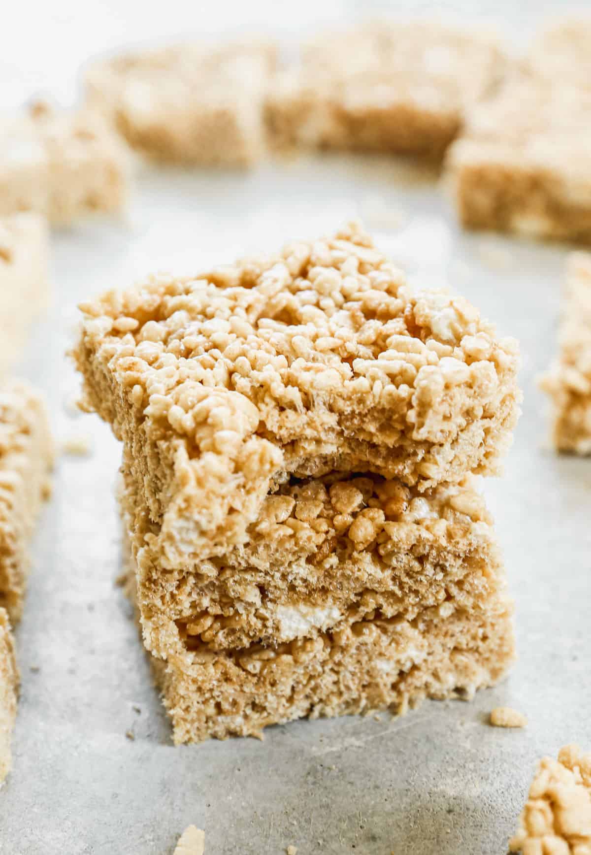 Three browned butter Rice Krispie Treats stacked with a bite taken out of the top one.