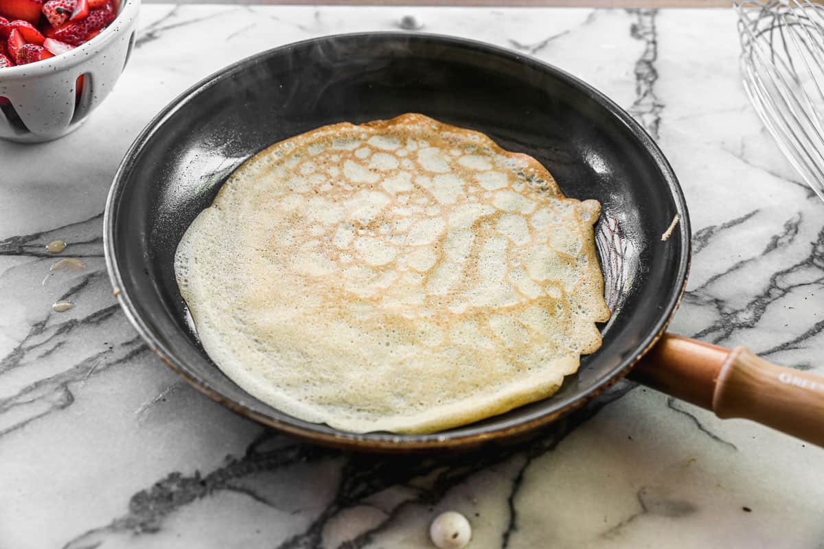 A crepe flipped over in a skillet, showing the side that is golden brown.