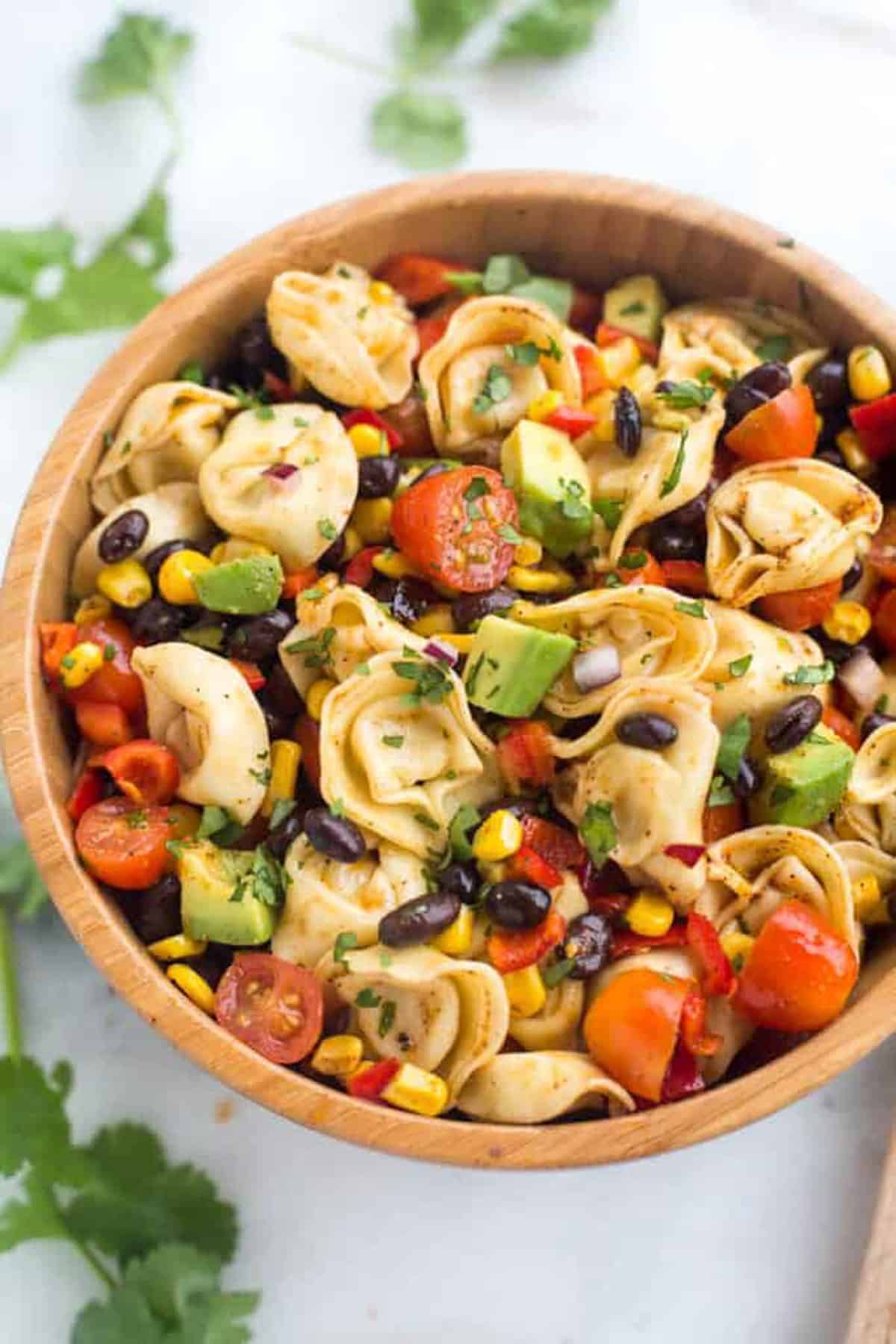 A Tortellini Pasta Salad with tomatoes, corn, black beans, and avocado in a wooden bowl.