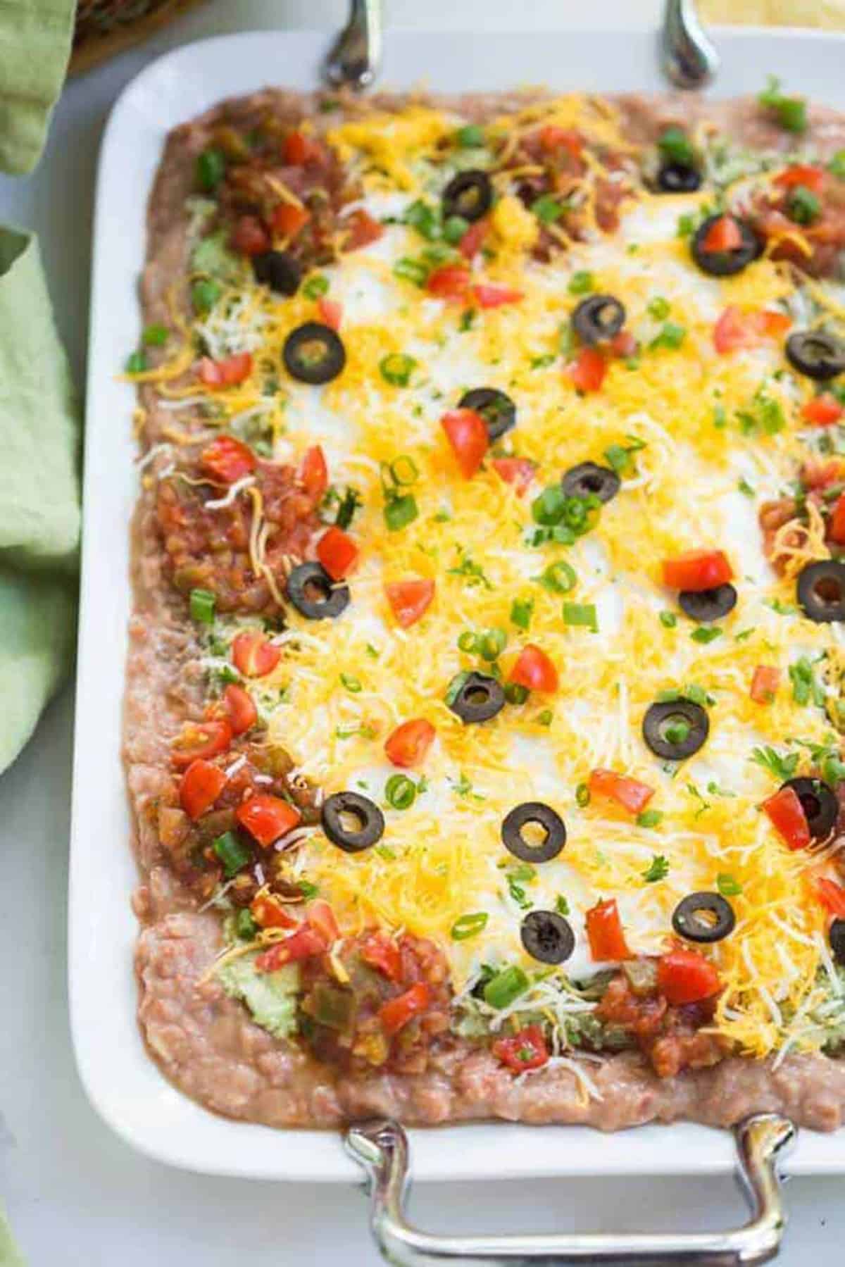 A pan filled with 7-layer Bean dip, ready to eat with chips.