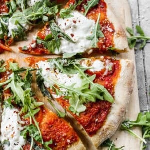 The best Burrata Pizza recipe topped with arugula and cut into slices on a wooden cutting board.