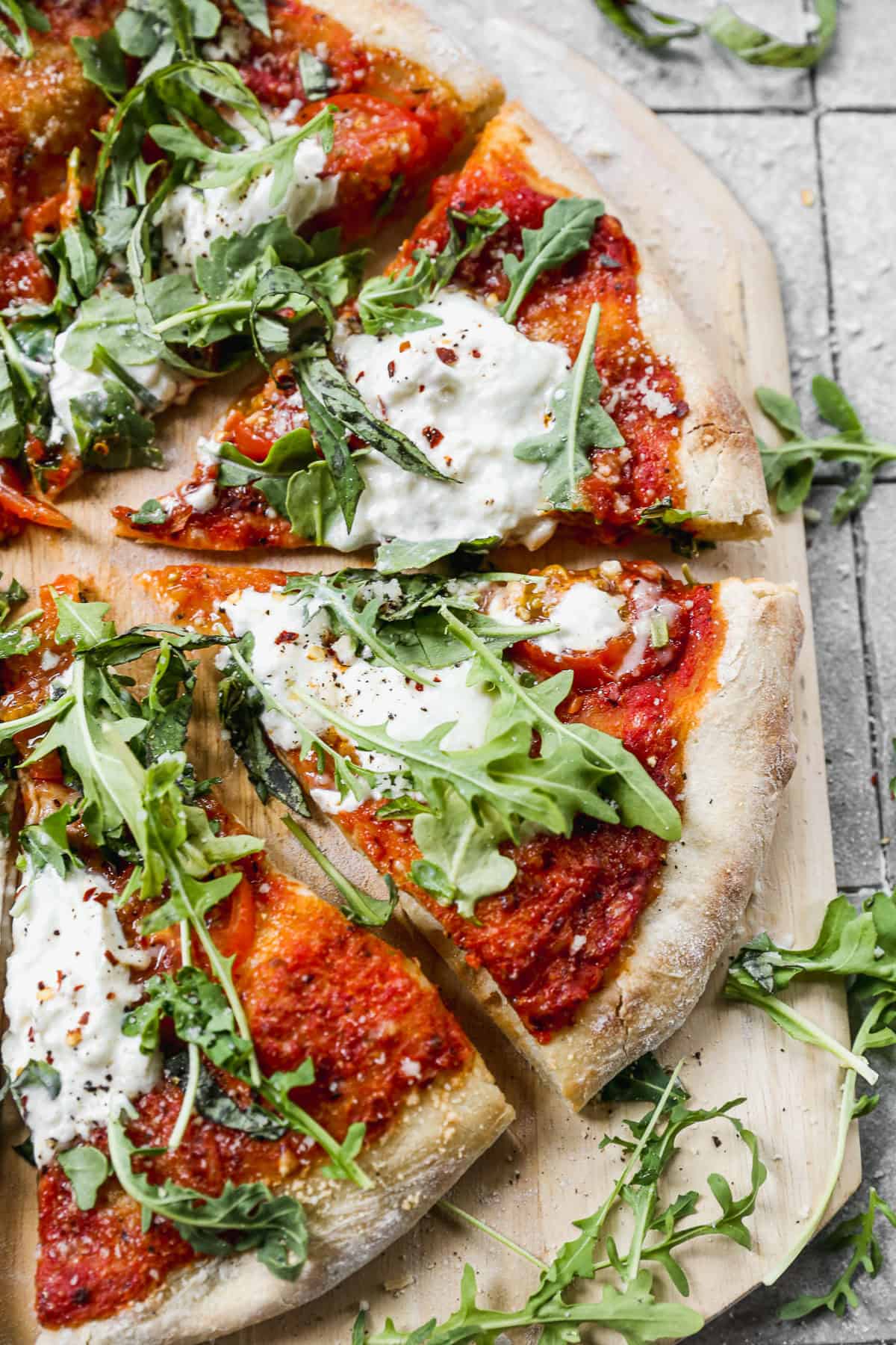 The best Burrata Pizza recipe topped with arugula and cut into slices on a wooden cutting board.