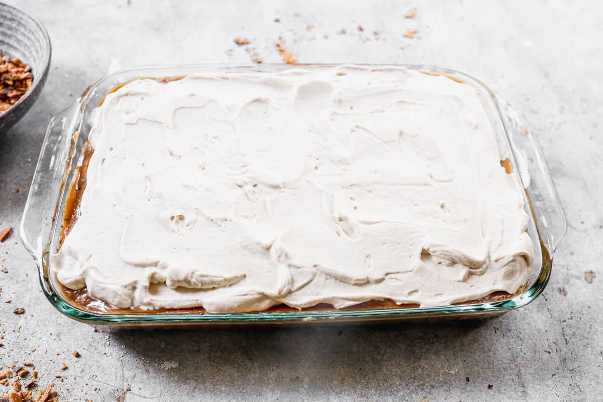 A 9x13 pan of a homemade Butterfinger Cake recipe, topped with peanut butter whipped cream.