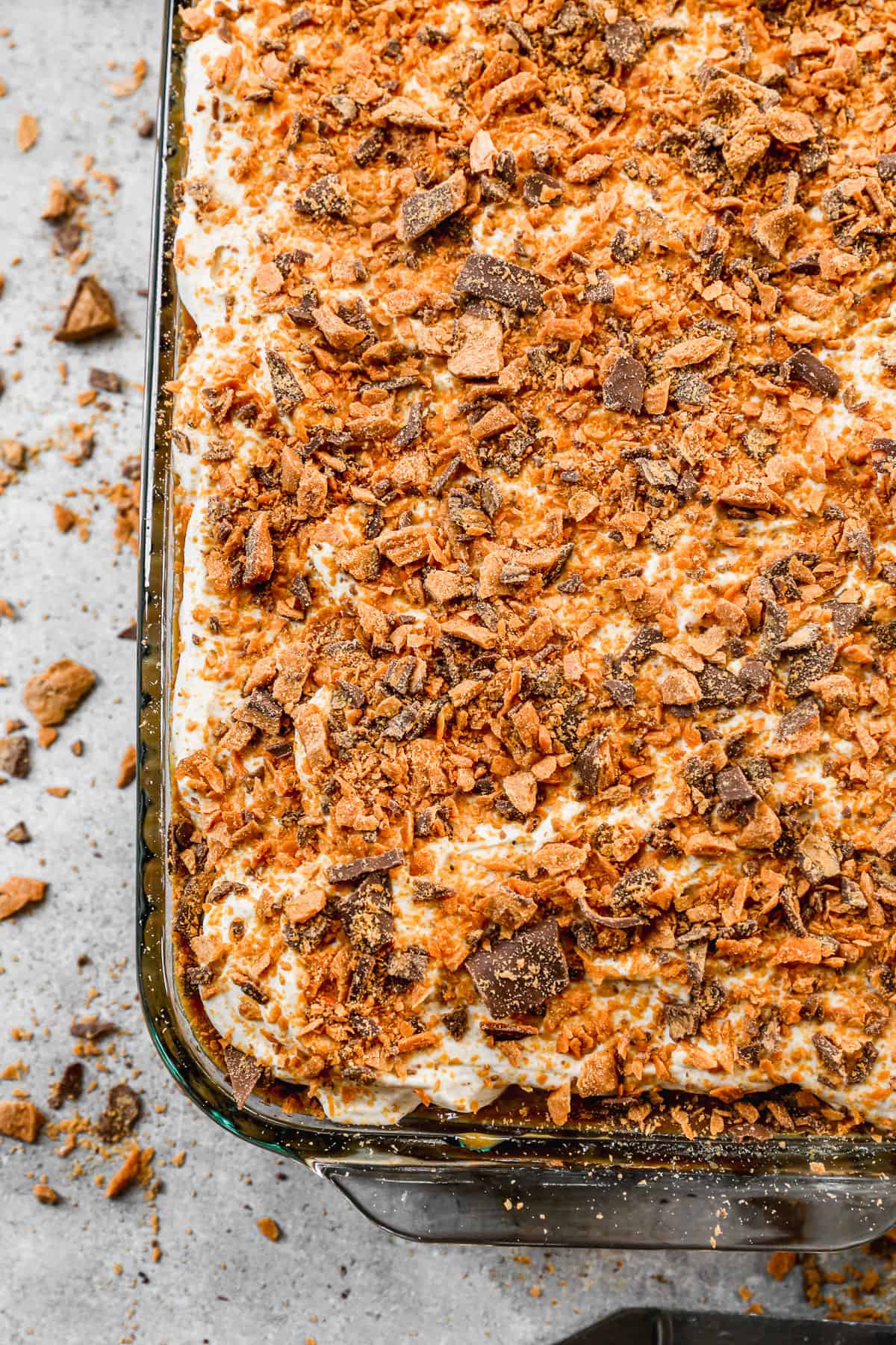 A close up image of an easy Butterfinger Poke Cake recipe with chopped butterfingers on top, ready to slice.