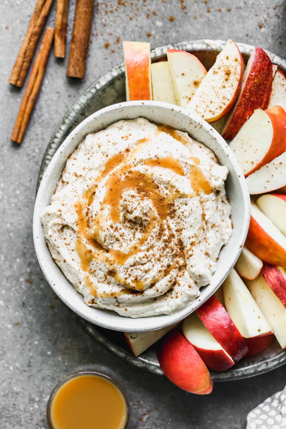 A bowl of Caramel Apple Dip, topped with caramel sauce and cinnamon, with sliced apples on the side.