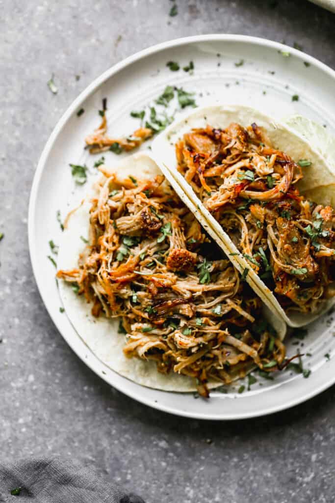 Two of the best carnitas recipe on a plate, topped with fresh cilantro.