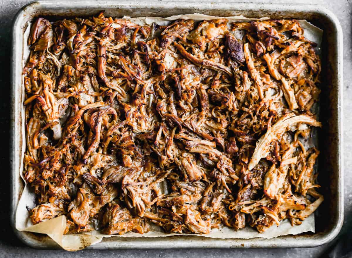A baking sheet lined with parchment paper then a single layer of pork carnitas meat, broiled.