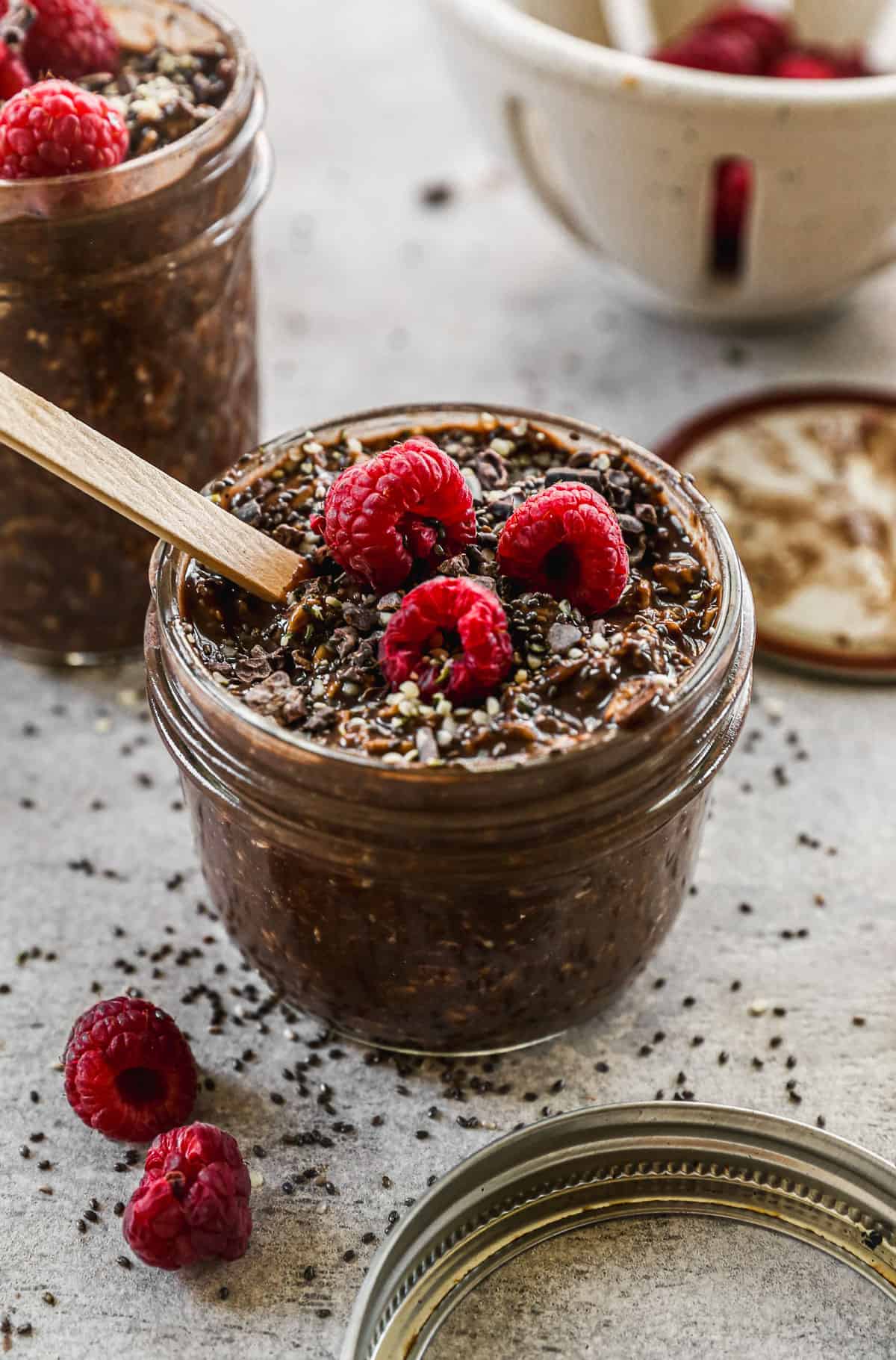 A glass jar filled with chocolate overnight oats, topped with cocoa nibs and fresh raspberries.