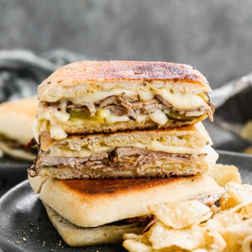 A traditional Cuban Sandwich sliced in half and placed on top of another sandwich, made with ciabatta rolls.
