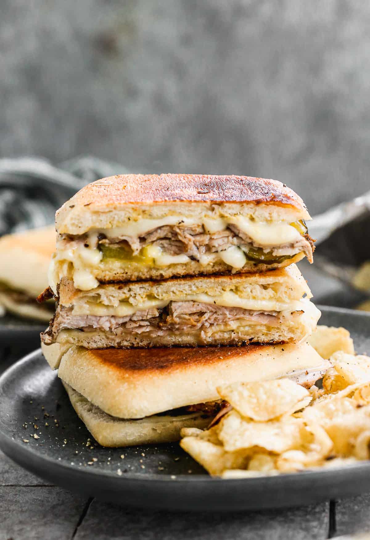 A traditional Cuban Sandwich sliced in half and placed on top of another sandwich, made with ciabatta rolls.