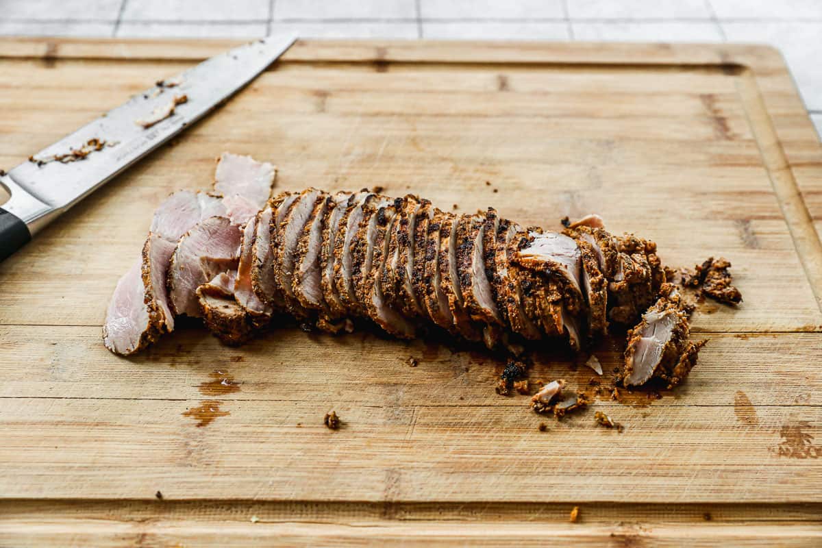 A cooked pork tenderloin sliced on a cutting board for a Cubano sandwich.