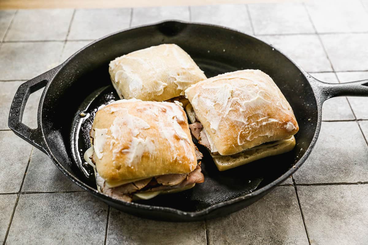 Three easy Cuban Sandwiches assembled and being cooked in a hot cast iron skillet.