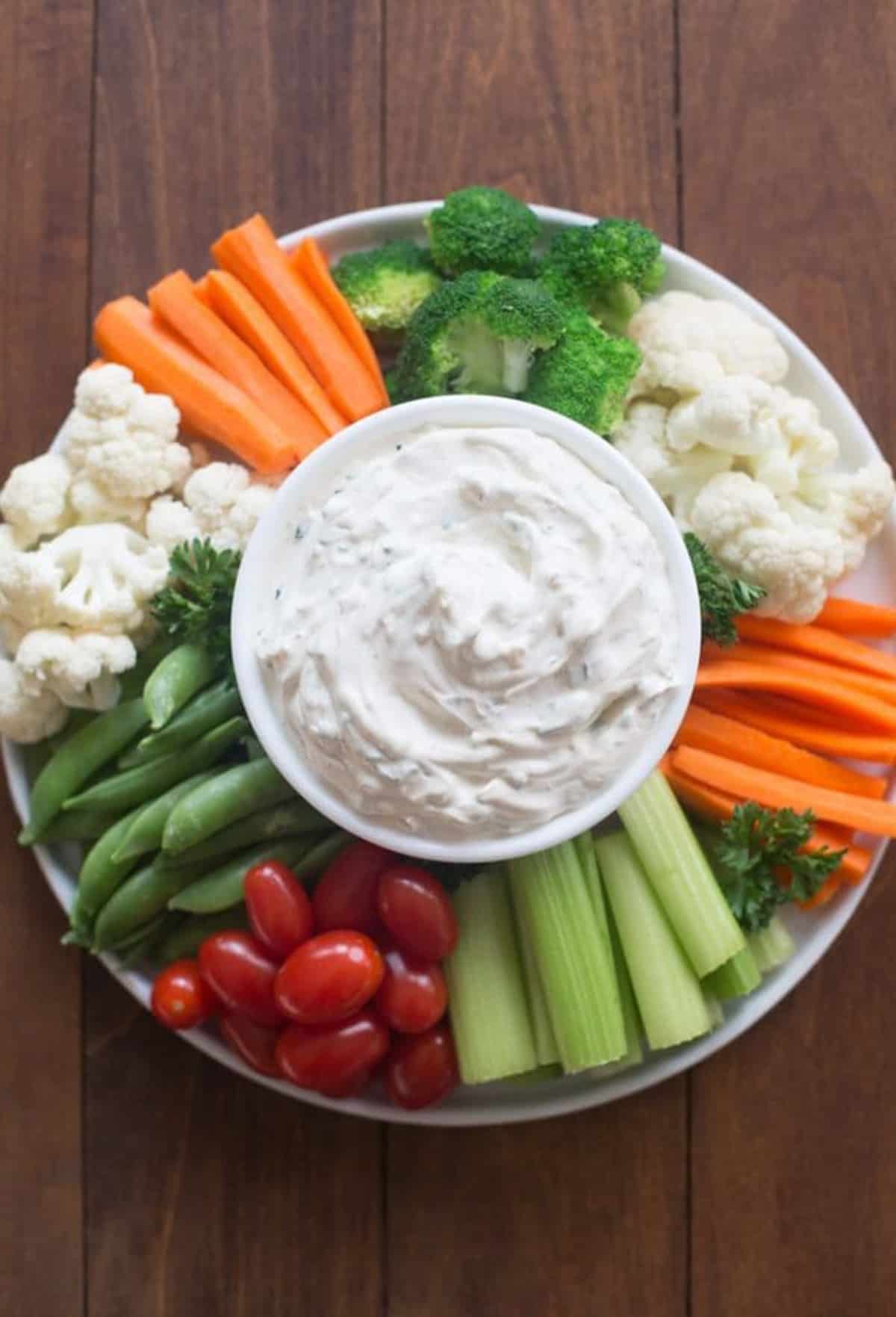 A platter of fresh cut vegetables with a bowl of vegetable dip in the center.