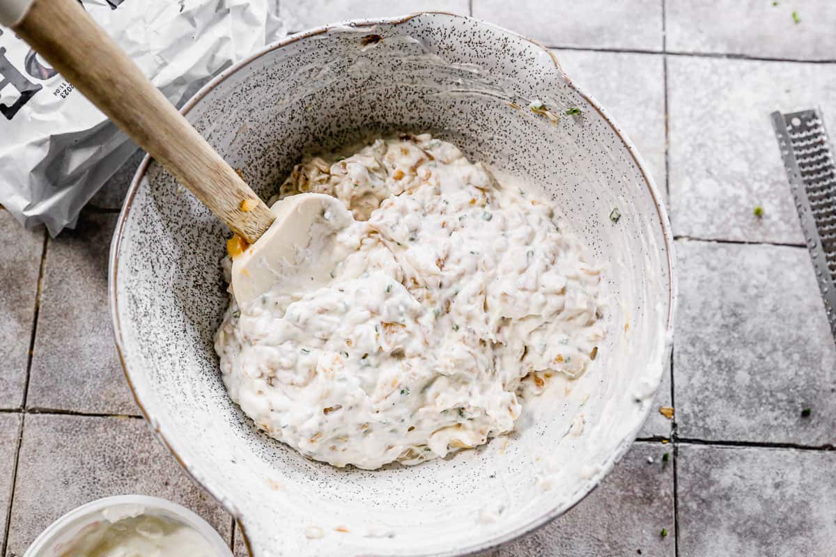 The best onion dip recipe in a mixing bowl with a rubber scraper.