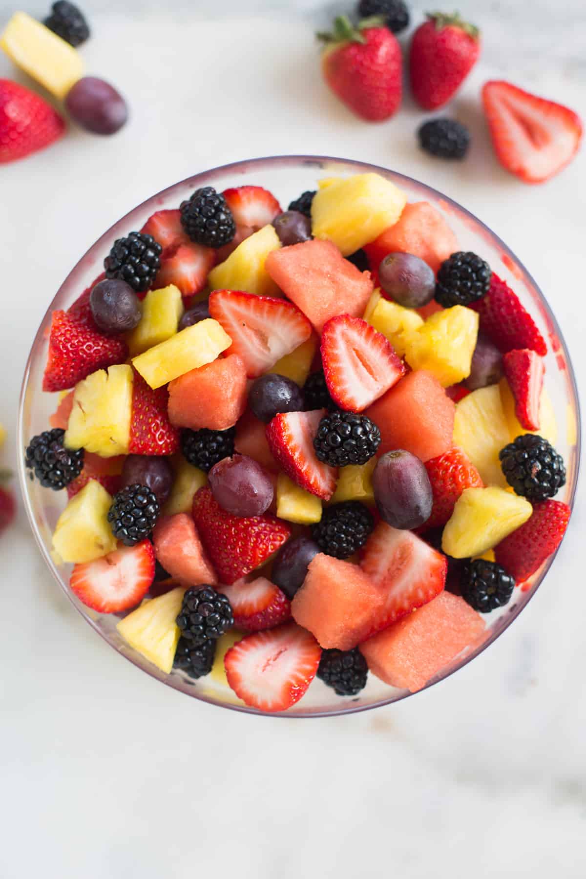A bowl of sliced fruit for a fruit salad, including: strawberries, watermelon, pineapple, grapes, and blackberries.