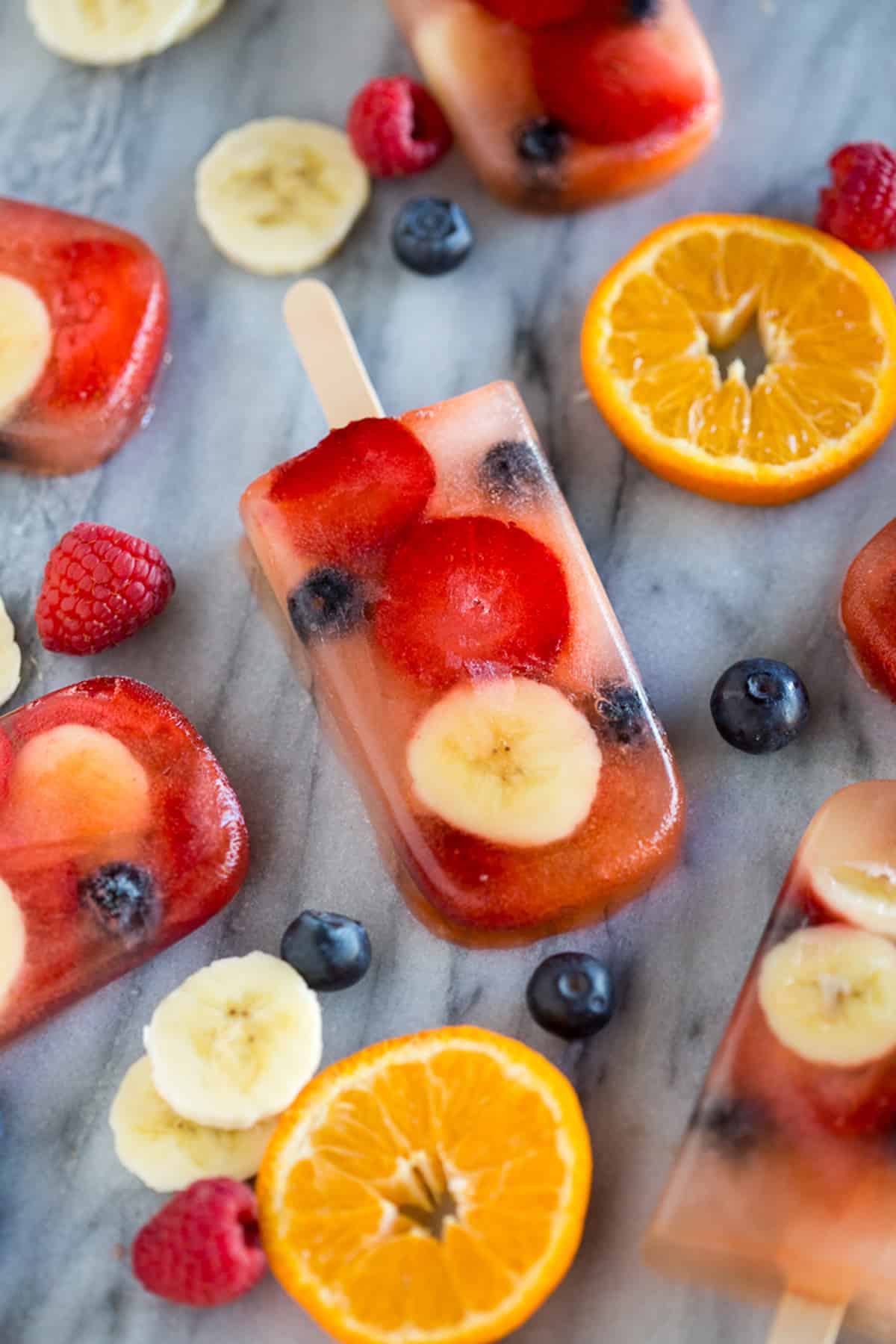 Homemade fruit pops on a counter top surrounded by more popsicles and fresh fruit. 