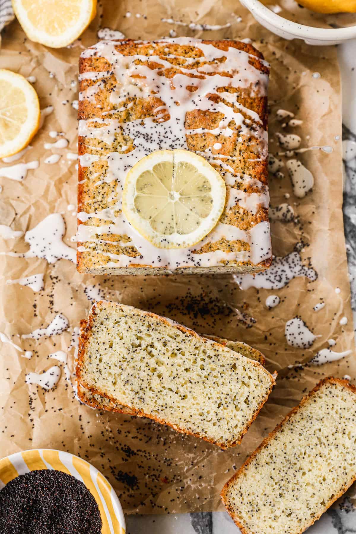 A loaf of homemade Lemon Poppy Seed Bread wiht lemon glaze and a slice of lemon on the top with a couple slices cut and ready to eat.