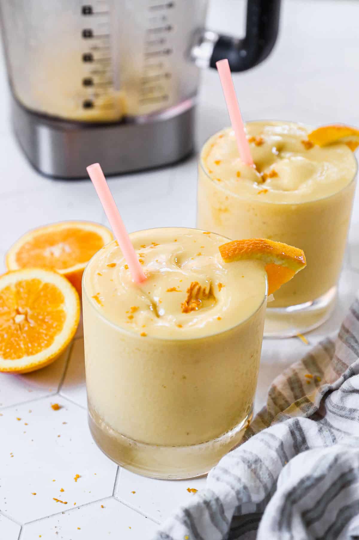 An easy Orange Julius recipe poured in two short glasses and topped with orange zest and a pink straw.
