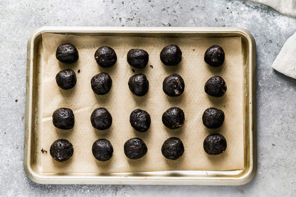 A baking sheet lined with parchment paper with Oreo truffles rolled into balls, ready to be dipped into chocolate.