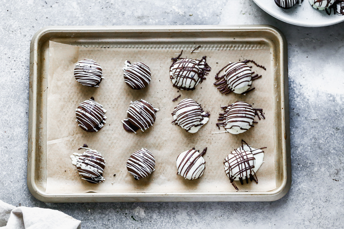 Oreo truffle balls on a baking sheet after being dipped in milk and white chocolate wafers and drizzled with melting chocolate.