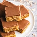 A stack of chewy peanut butter bars topped with a layer of peanut butter and a chocolate frosting on a plate to share.