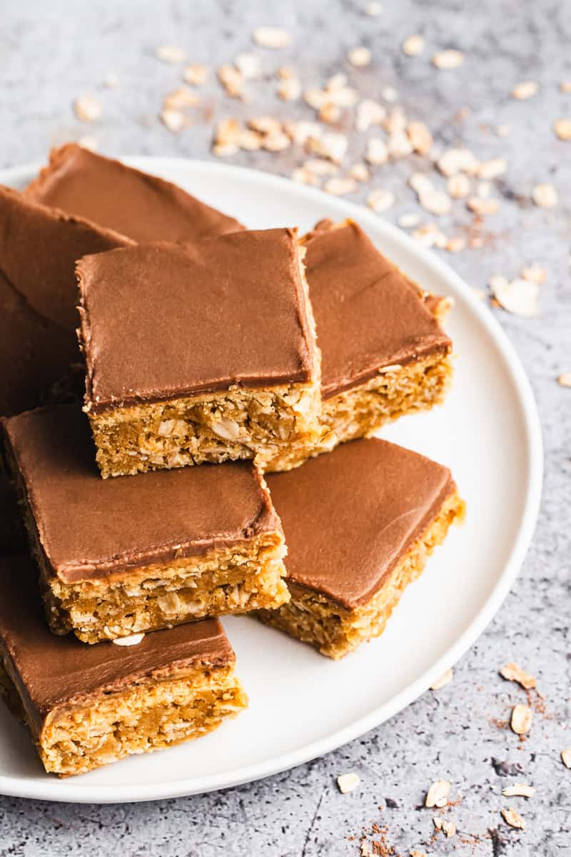 A stack of chewy peanut butter bars topped with a layer of peanut butter and a chocolate frosting on a plate to share.