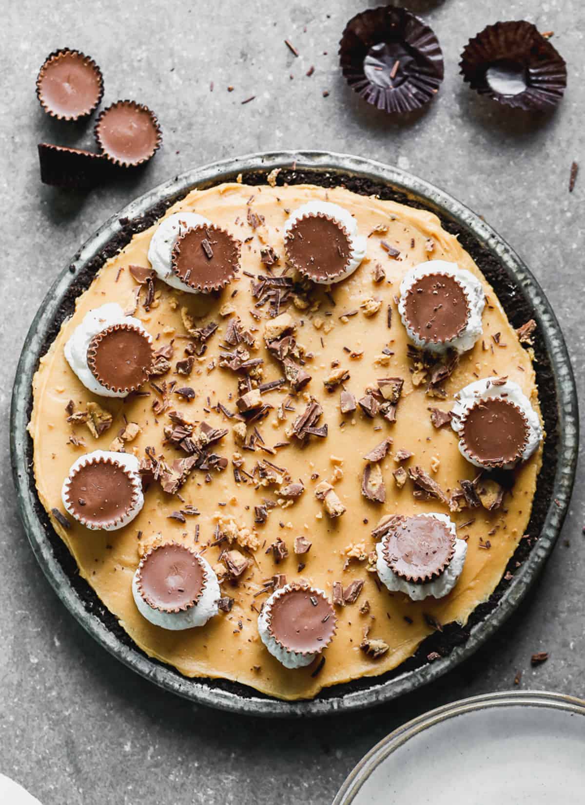 The best no bake Peanut Butter Pie, topped with whipped cream dots, Reeses peanut butter cups, and chopped butterfinger.
