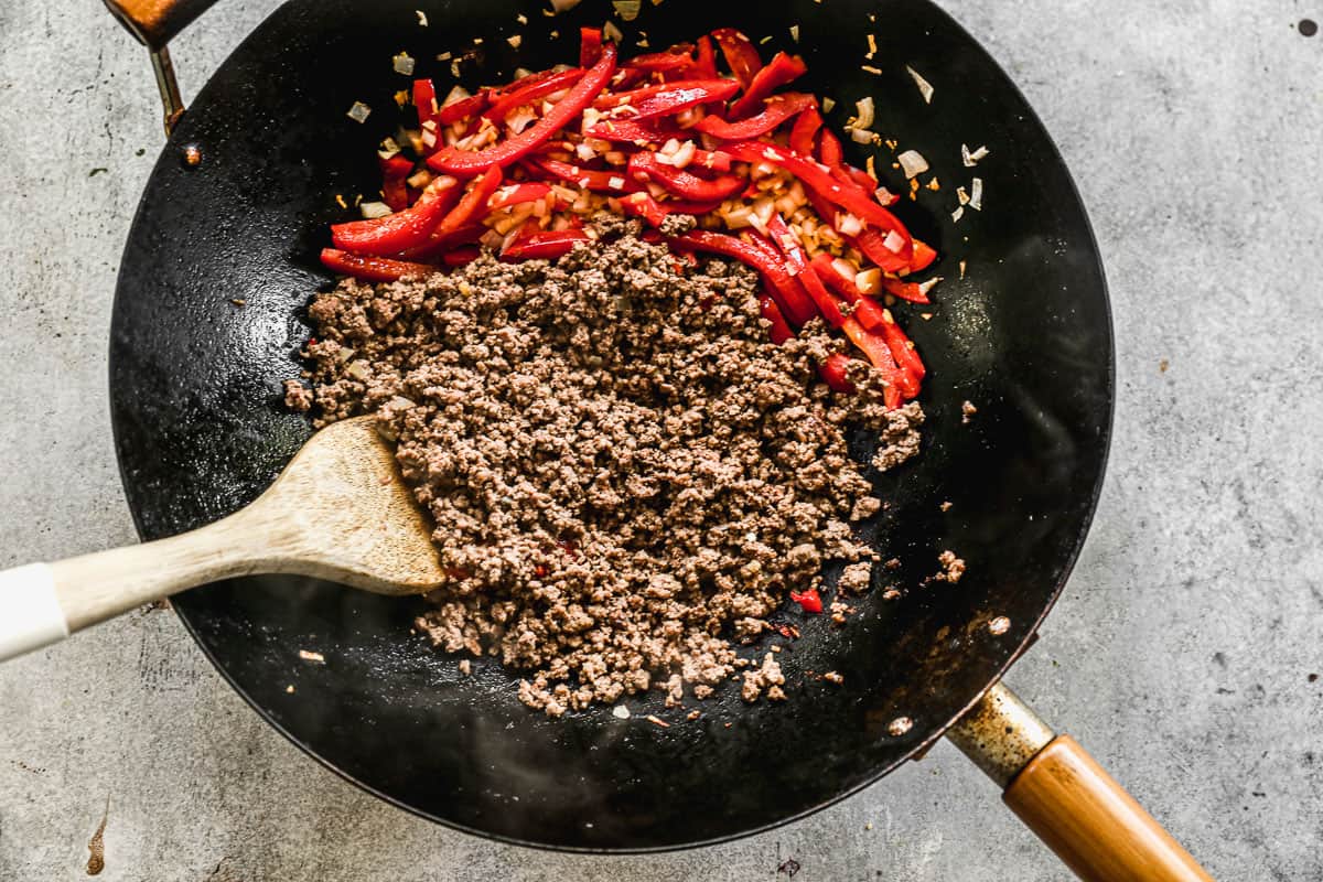 A wok filled with cooked ground beef, red peppers, shallots, and garlic to make Thai Basil ground beef.