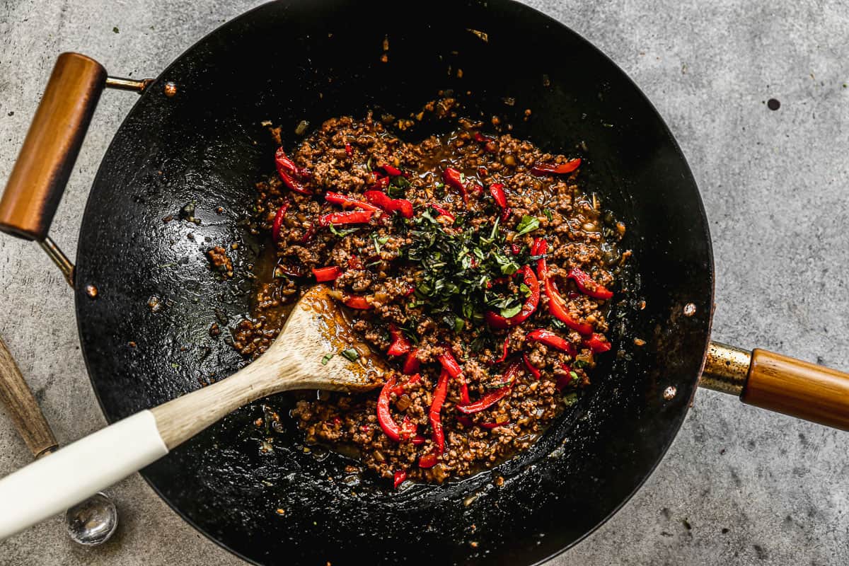 A Thai Basil Beef stir fry in a large wok with fresh basil on top.