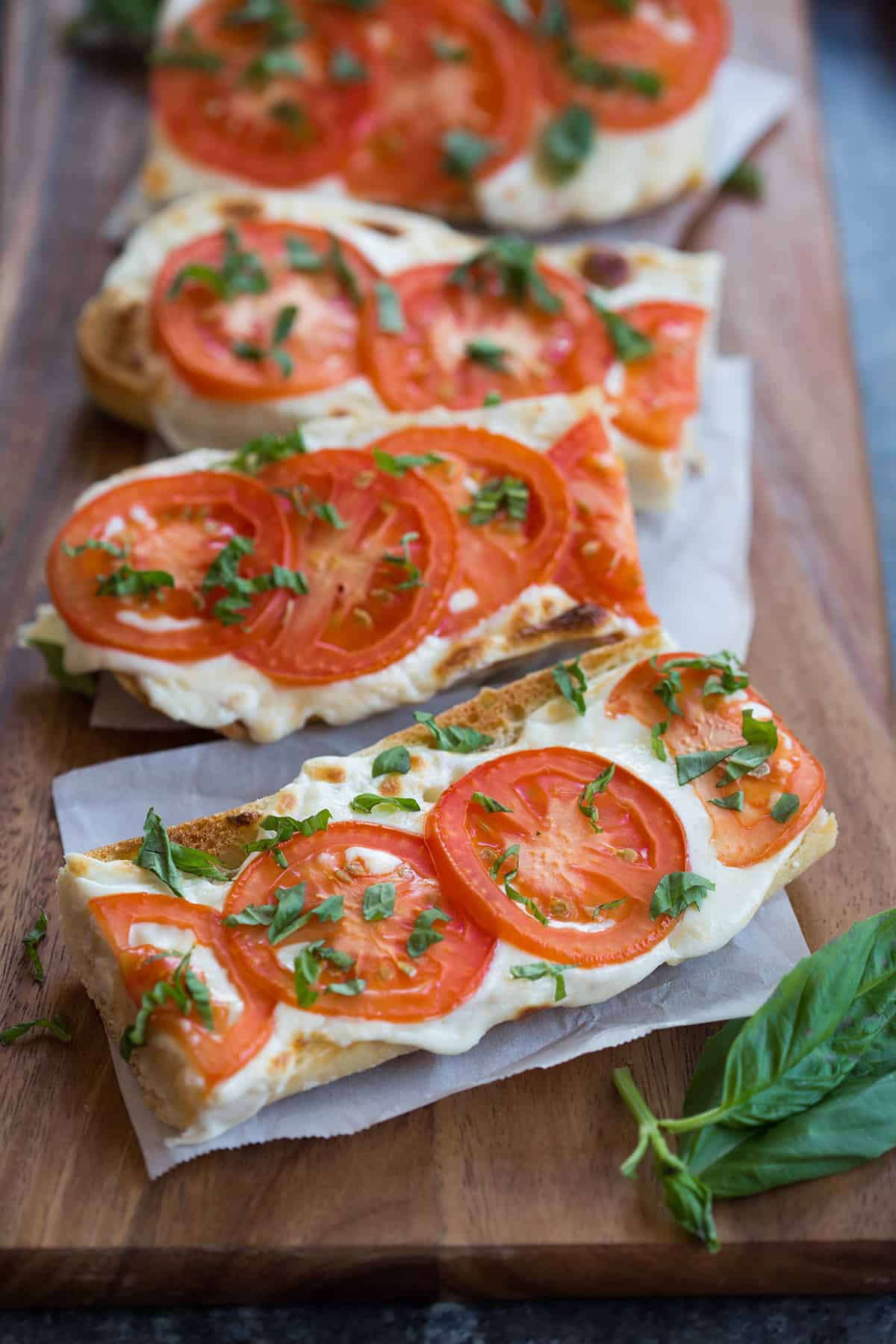 Tomato and Basil toasts covered in melted mozzarella cheese, sliced tomatoes, and sprinkled with fresh basil.