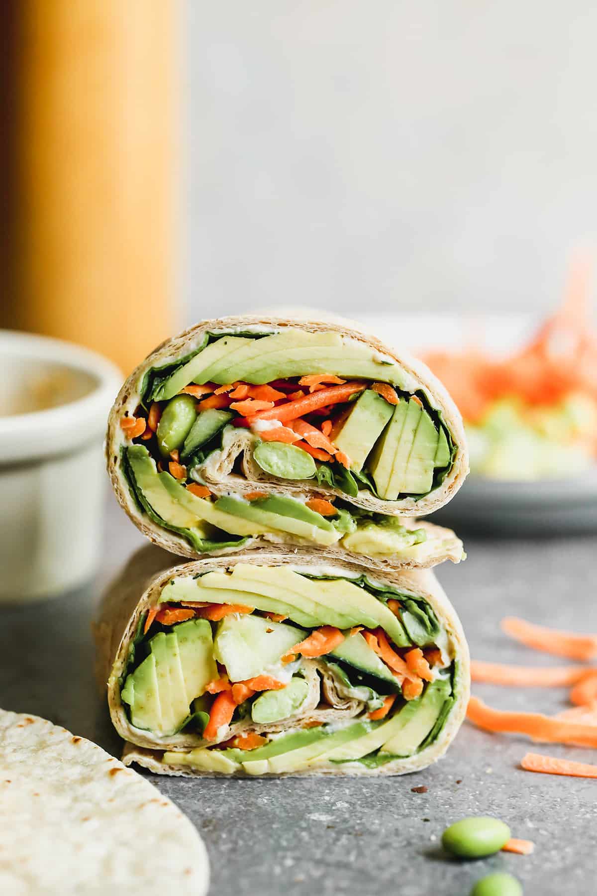 A veggie wrap sliced in half and stacked on top of each other to show the lettuce, avocado, cucumber, snap peas, and shredded carrots inside.