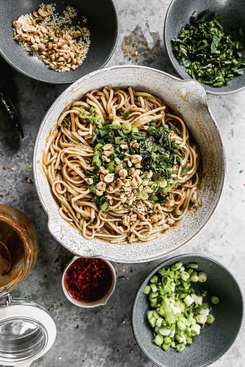 A serving bowl with warm homemade peanut noodles, garnished with fresh herbs and green onions. 