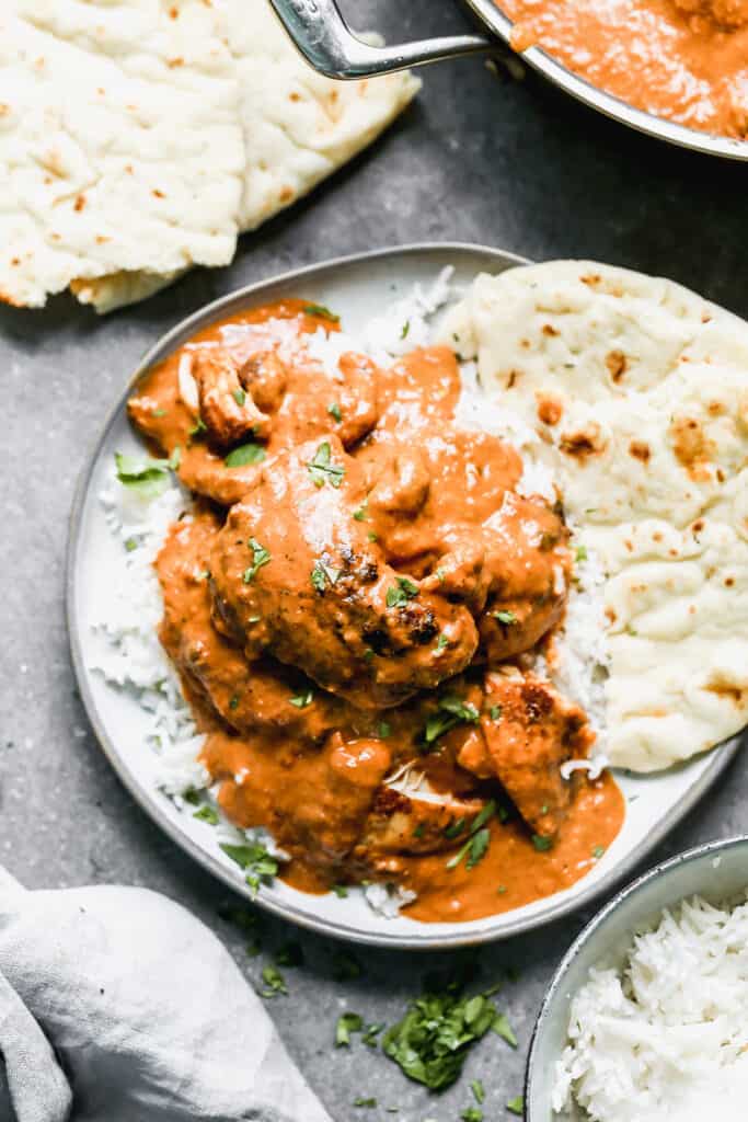 An easy Chicken Tikka Masala recipe served on a plate over rice and a piece of naan bread next to it.
