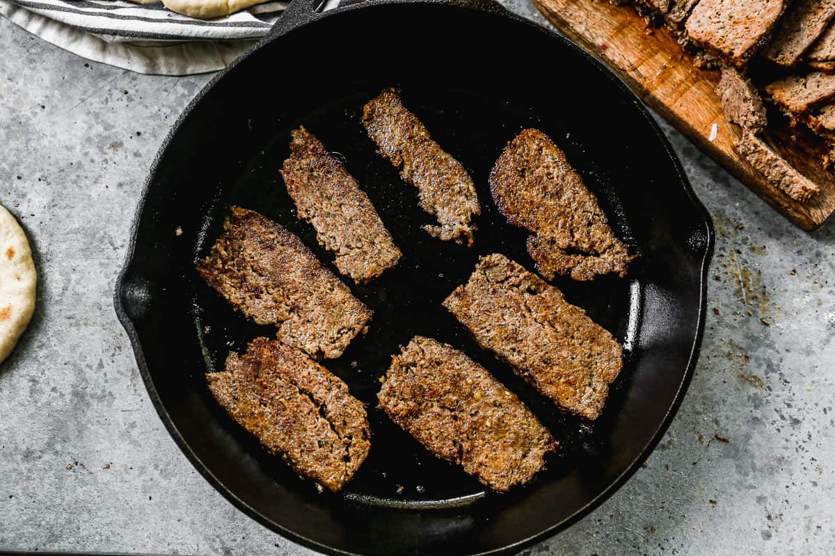 Slices of easy gyro meat being heated in a cast iron pan before being assembled into gyros.