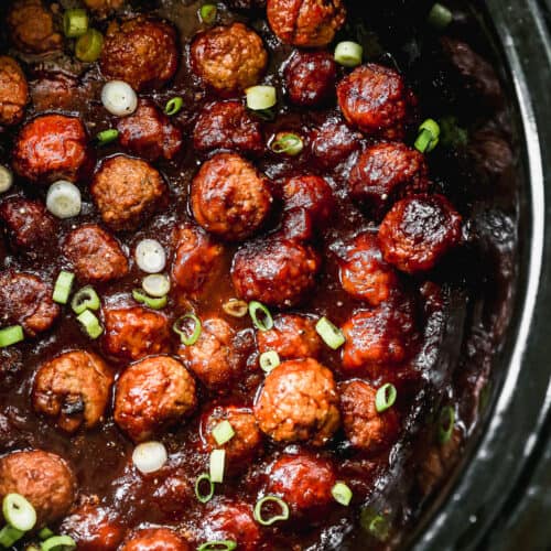 A crockpot hawaiian meatballs recipe in a crockpot and topped with green onions.