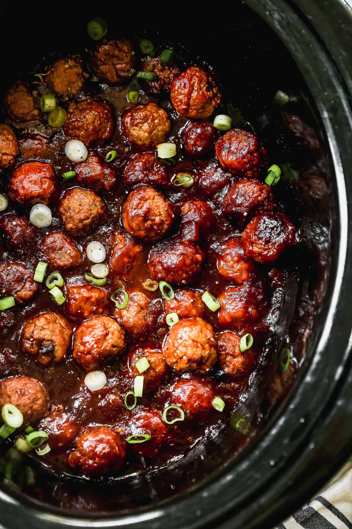 A crockpot hawaiian meatballs recipe in a slow cooker and topped with fresh chopped green onions.