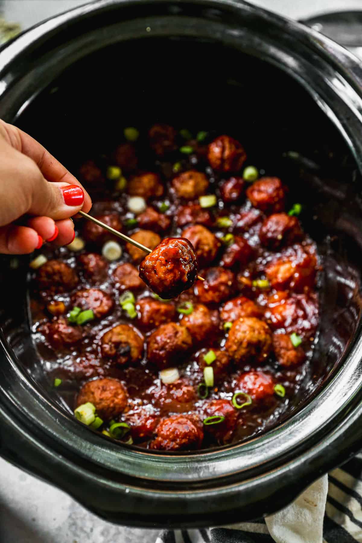 3 ingredients Hawaiian Meatballs in a crockpot and one meatball being lifted with a toothpick. 