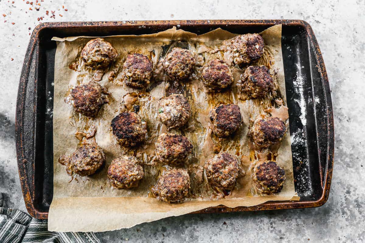 Meatballs on a parchment lined baking sheet, fresh out of the oven.