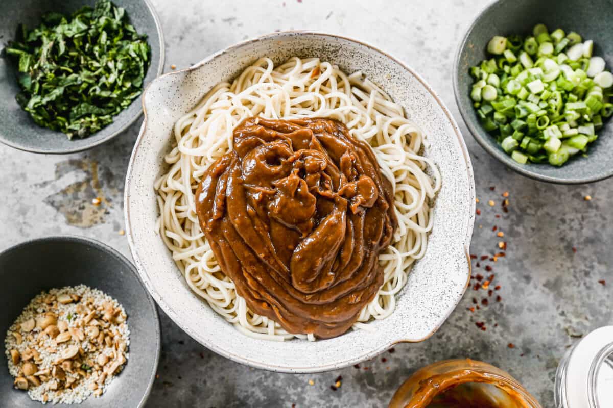 Peanut sauce poured on top of a bowl full of warm udon noodles.