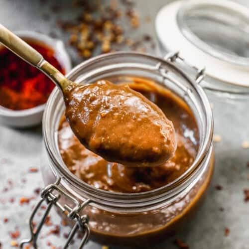 An easy Peanut Sauce recipe in a jar with a spoon lifting some up.