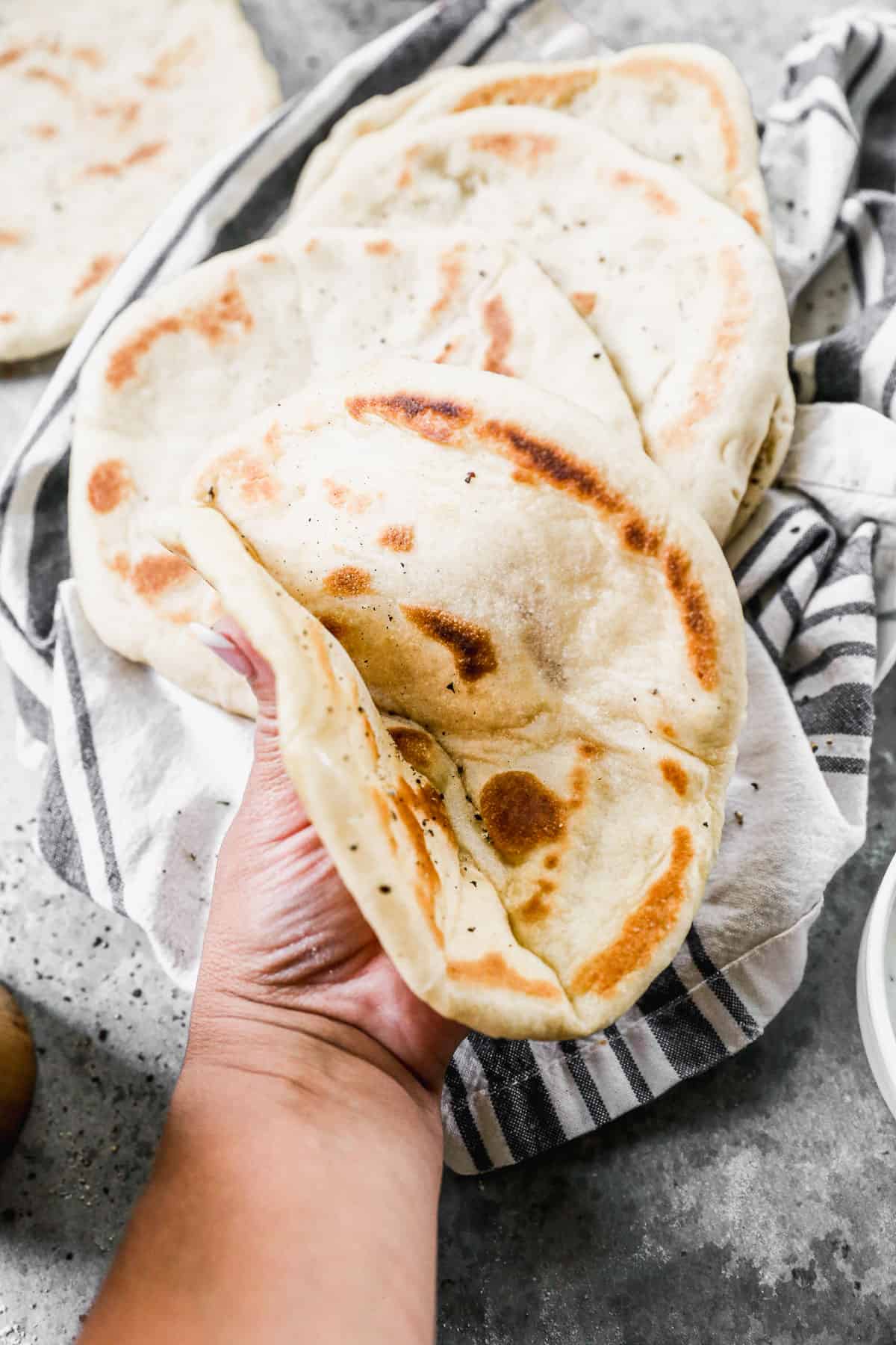 Someone folding a greek pita bread in half with a stack of easy pita breads behind.