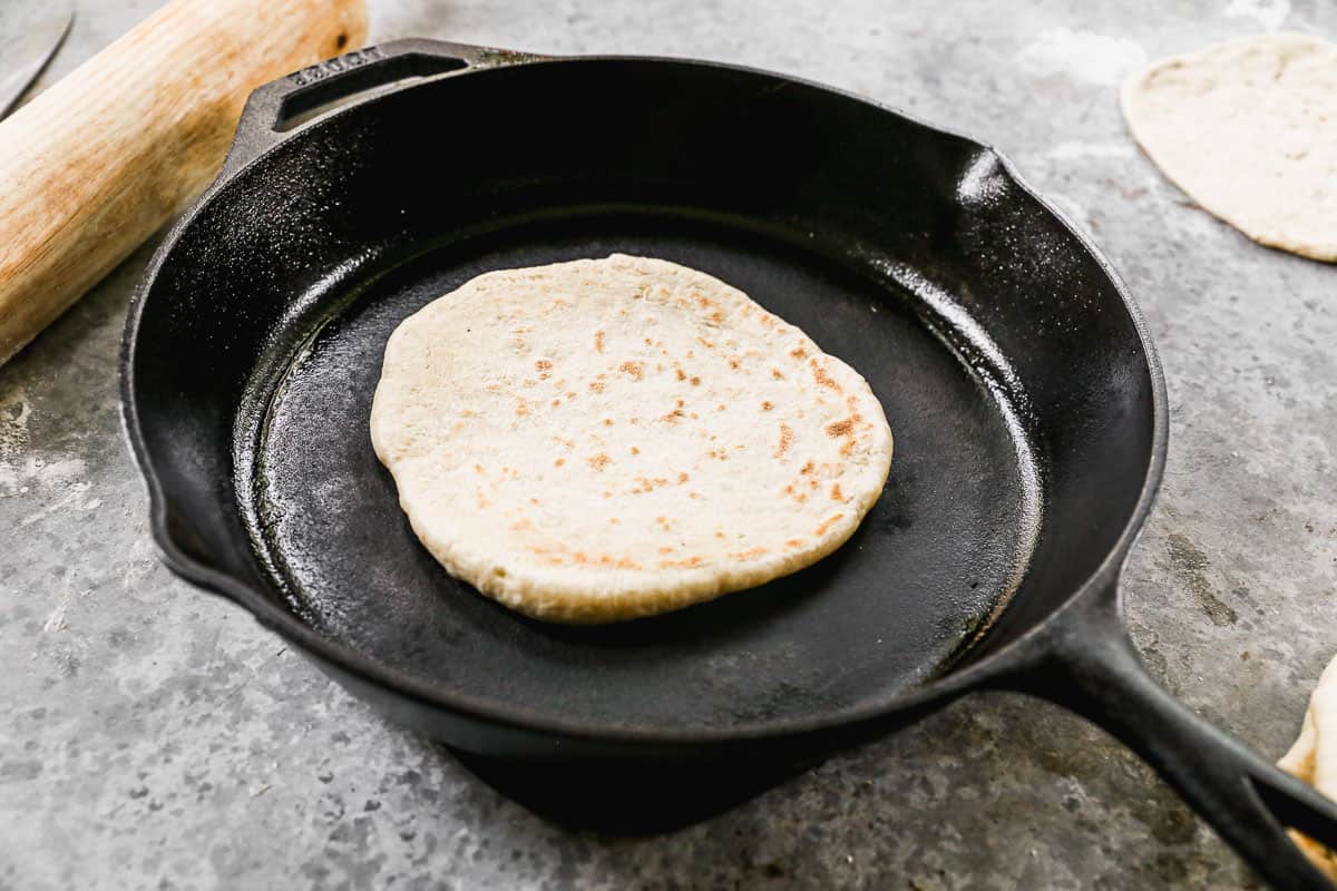 An easy pita bread recipe being cooked in a cast iron skillet.