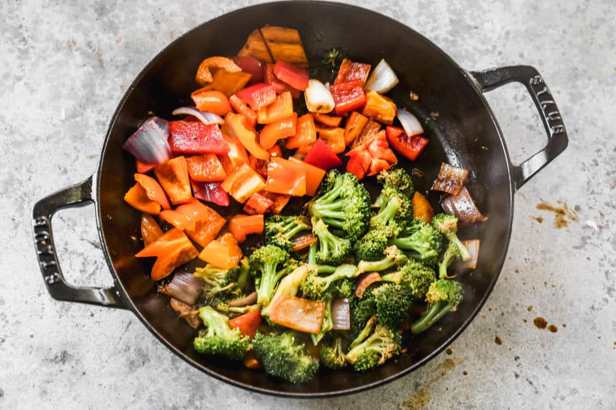 Chopped vegetables being sautéed in a skillet, including: red and orange bell peppers, red onion, and broccoli.