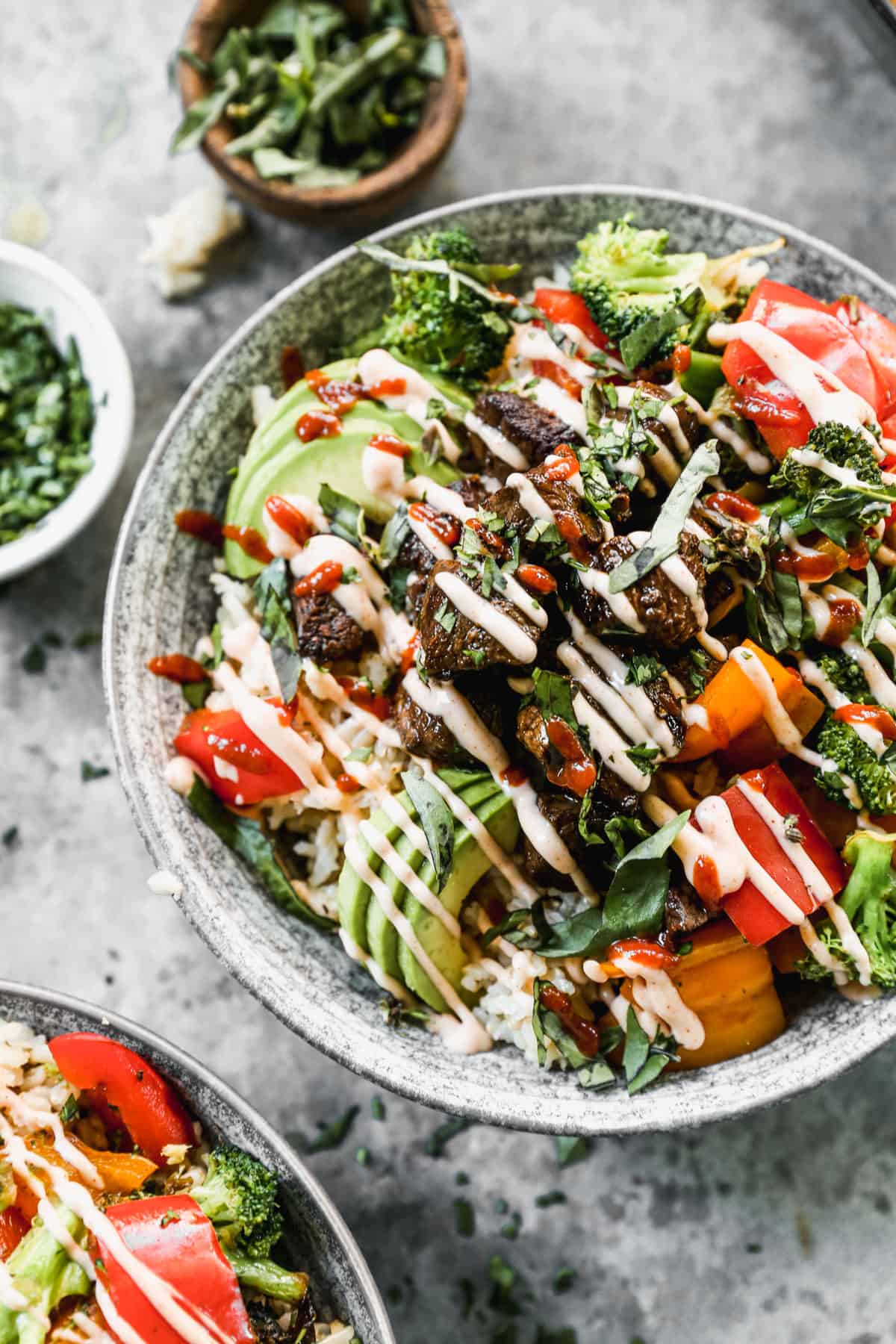 A close up image of a Yumm bowl assembled with steak and fresh sautéed vegetables on top of a bed of rice and topped with avocado and yum yum sauce.