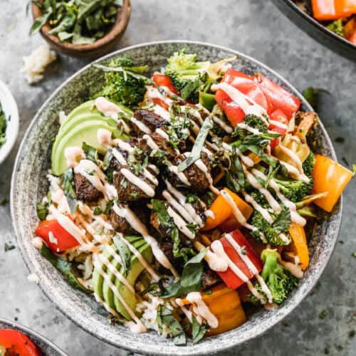 A Yum Yum Bowl recipe with a bed of rice topped with steak, bell peppers, broccoli, fresh avocado, and a drizzle of yum yum sauce.