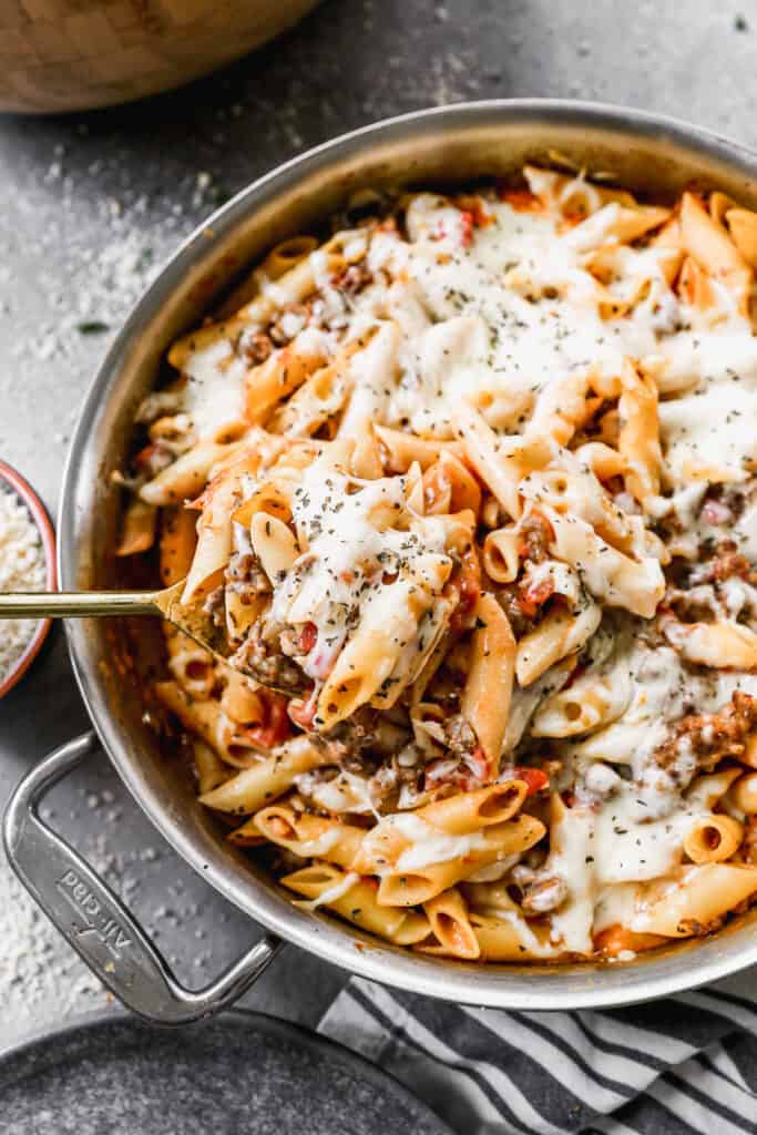 A homemade Baked Ziti recipe in a pan, with a spoonful being lifted.