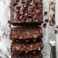 Moist chocolate banana bread baked in a loaf pan and sliced on parchment paper to reveal gooey melted chocolate chips inside.