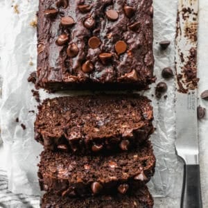 Moist chocolate banana bread baked in a loaf pan and sliced on parchment paper to reveal gooey melted chocolate chips inside.