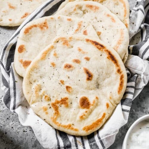 A stack of homemade pita bread on a dish towel, freshly cooked and ready to eat.